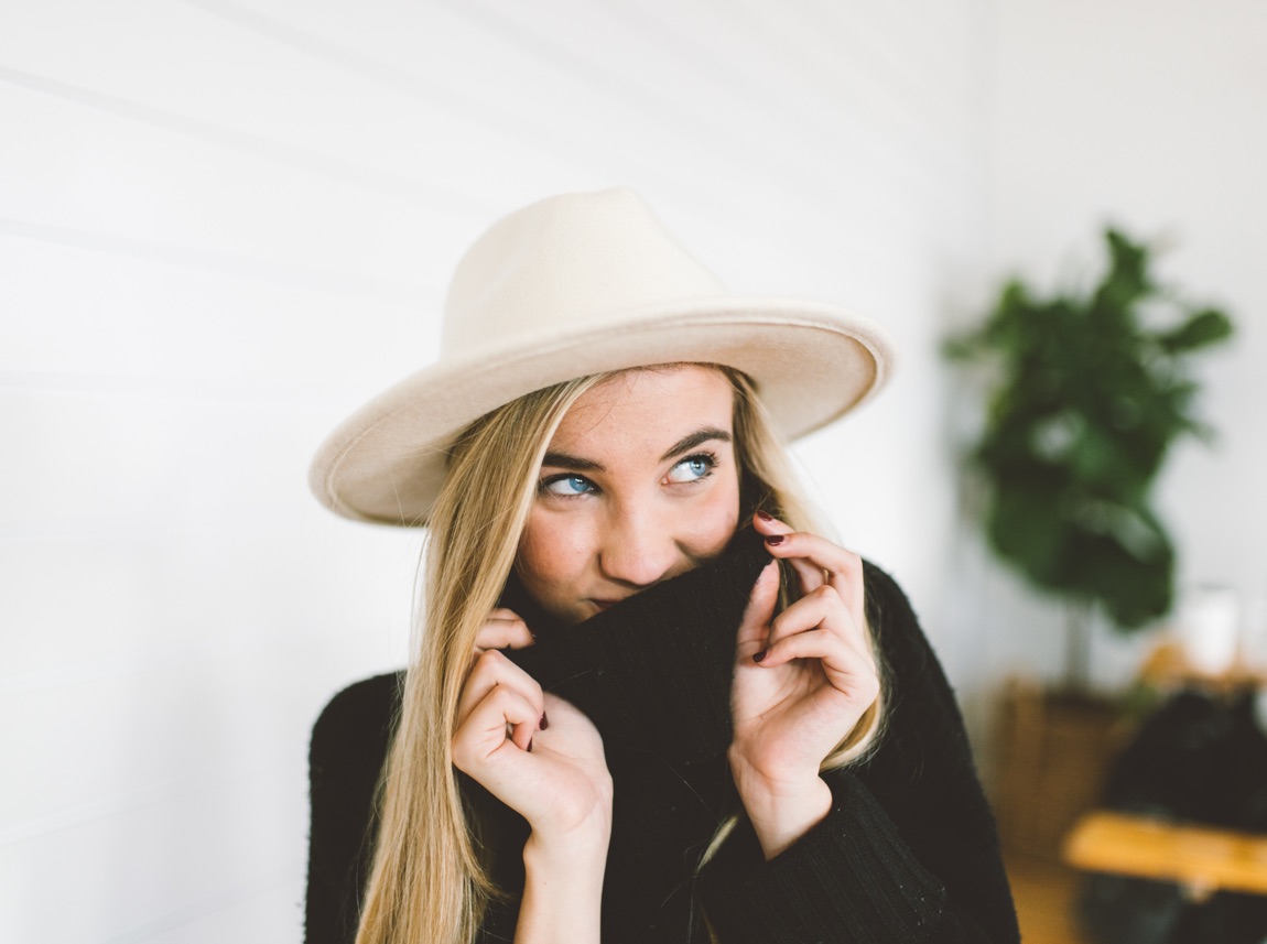 Young woman wearing a hat pulling her pullover over her mouth.