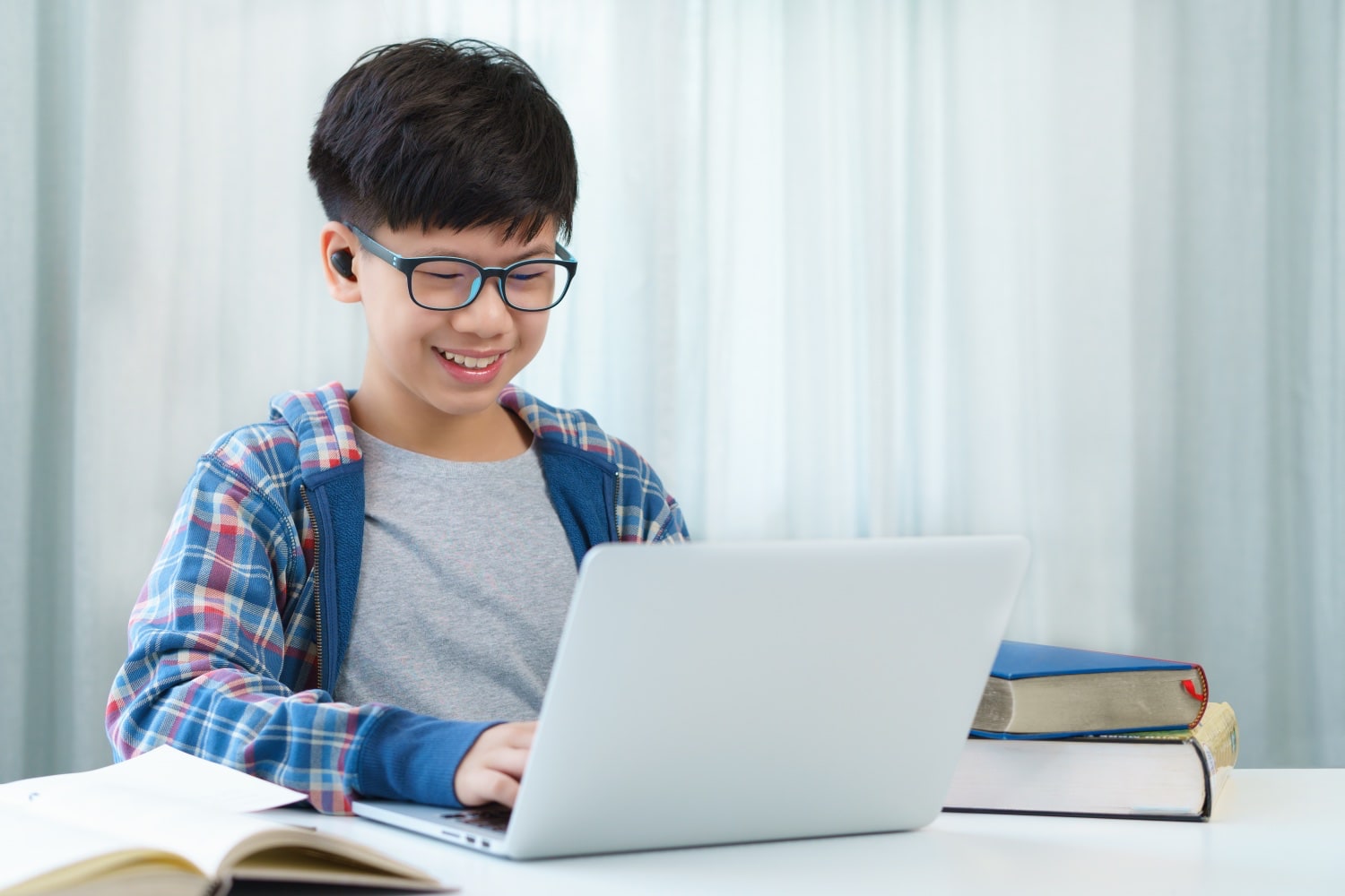 Asiatischer Junge mit Brille arbeitet am Notebook.