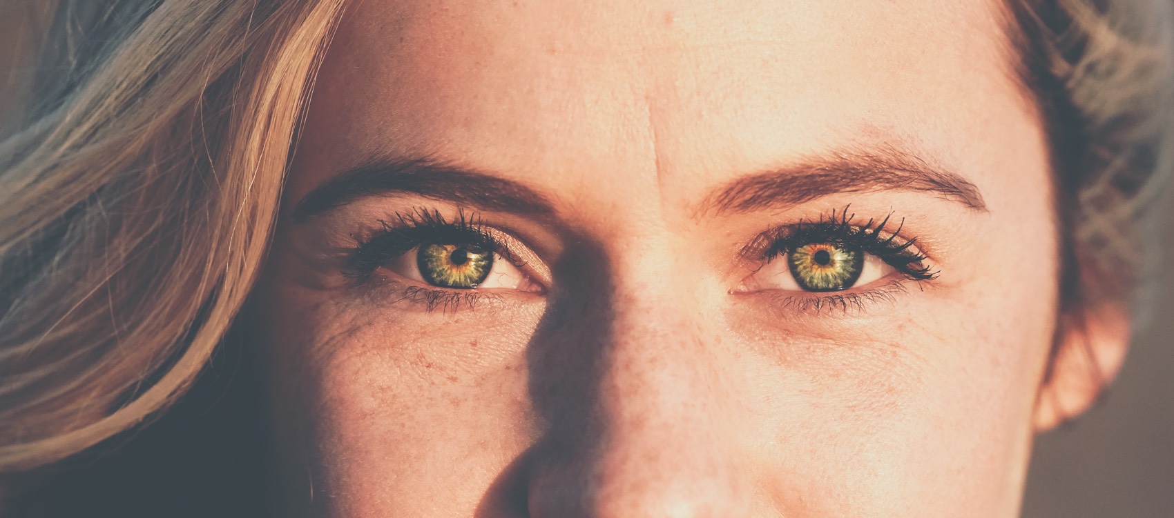 Eine Frau mit blonden Haaren und grünen Augen. Nase und Mund sind nicht sichtbar.