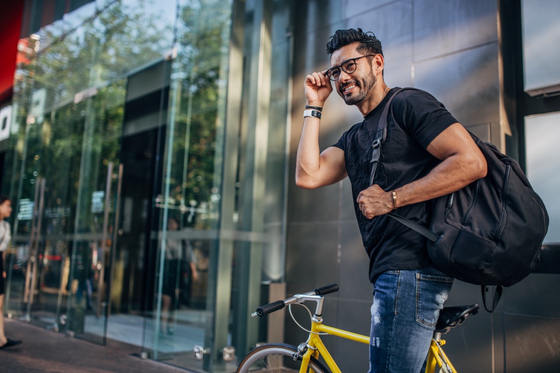 Junger sportlicher Mann mit Fahrrad setzt seine Brille nach dem Sport auf.