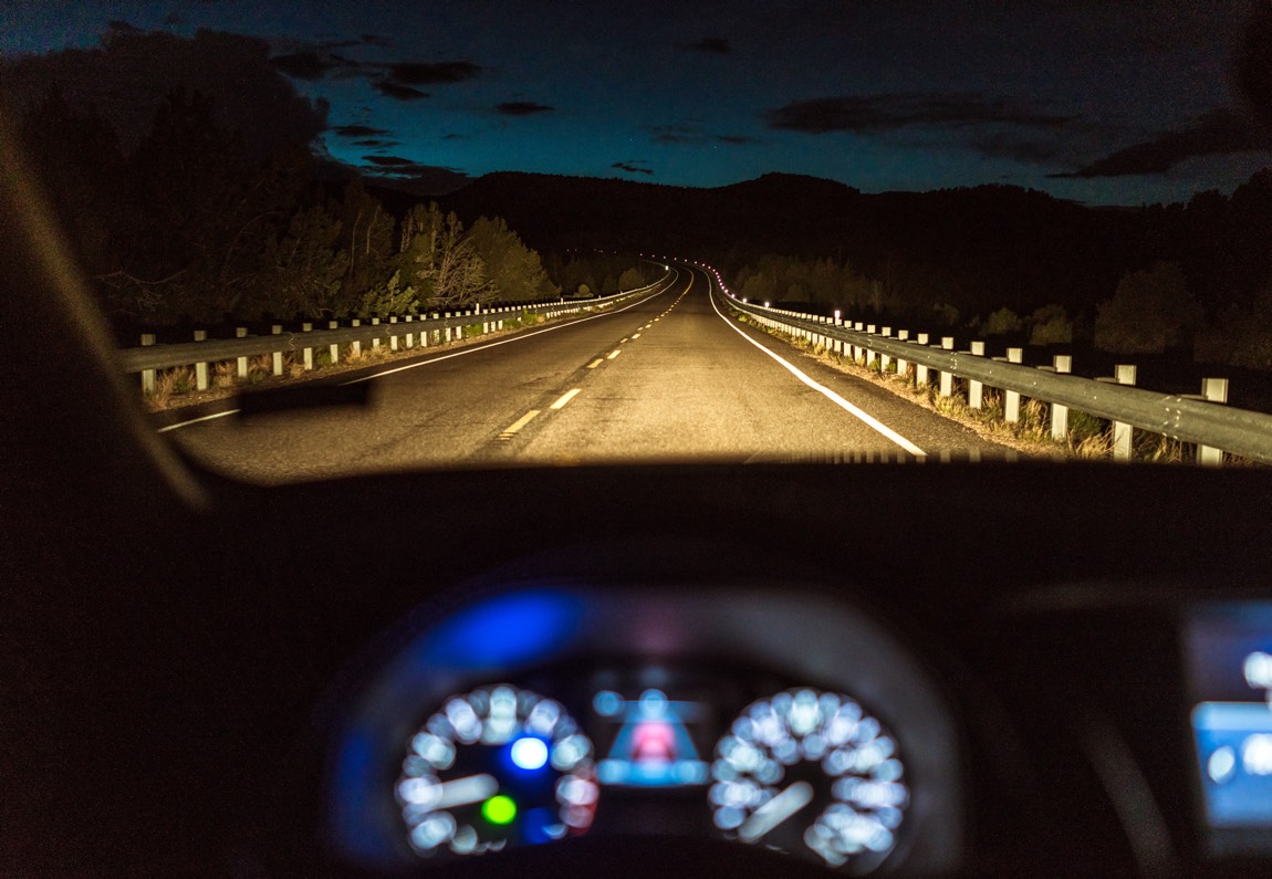 Blick auf einen unscharfen Tachometer und die Straße bei Nacht.