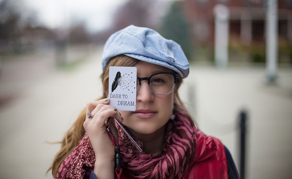 Frau hält sich eine Karte mit der Aufschrift “Dare to dream” vor das linke Auge.