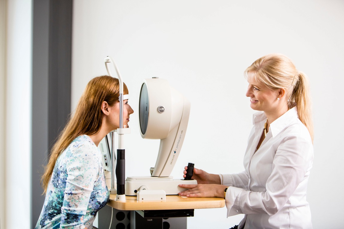 Eine Mitarbeiterin der Praxisu untersucht die Augen einer jungen Frau mit der Pentacam HR.