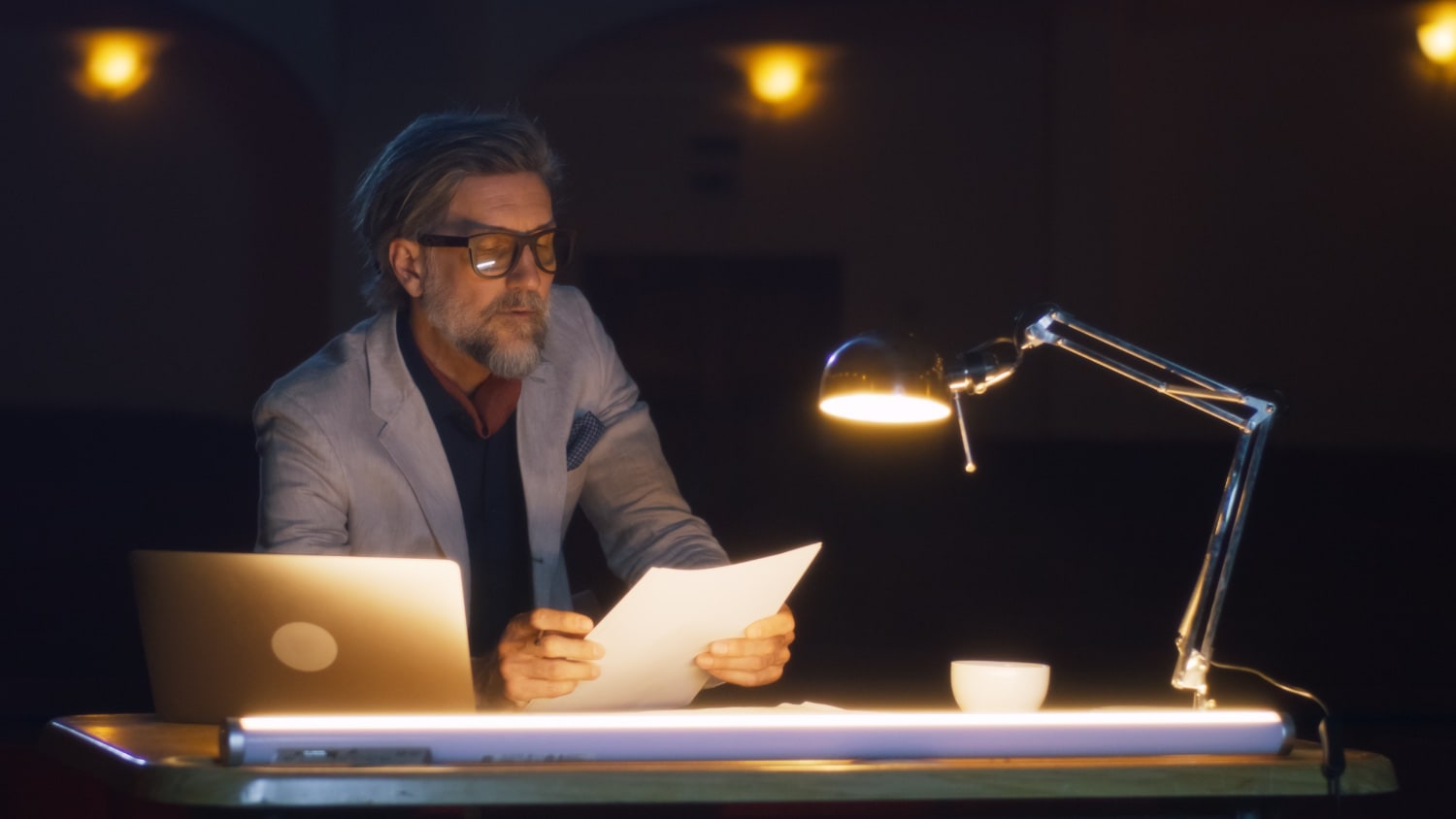 Mann mittleren Alters sitzt im Dunkeln am Schreibtisch mit heller Schreibtischlampe.