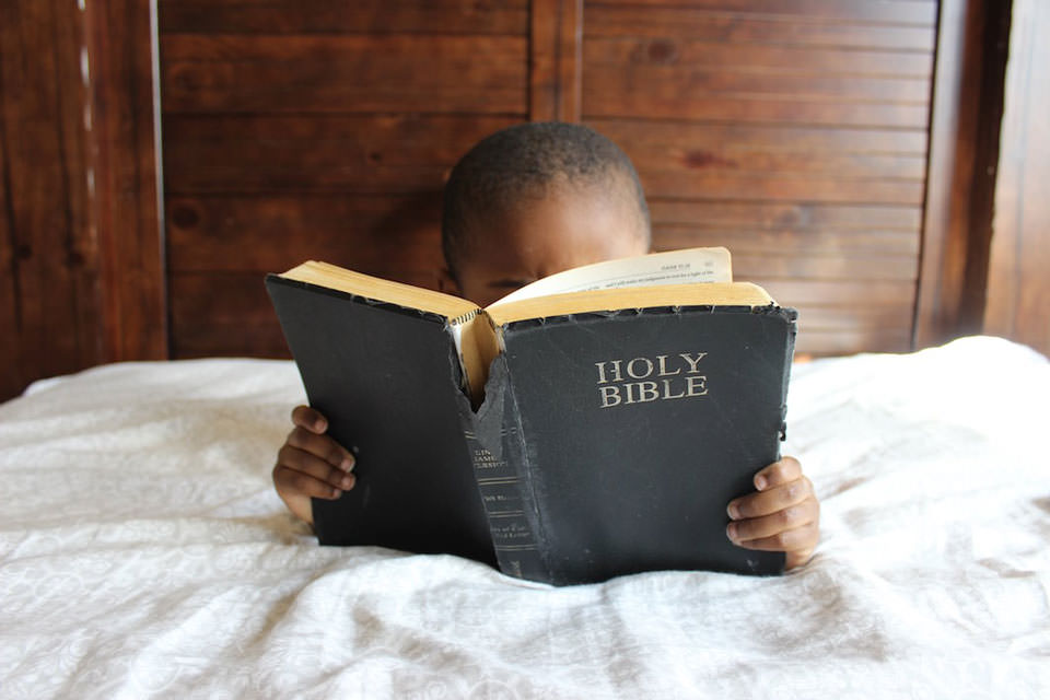 Kleiner Junge im Bett, der die Bibel liest.