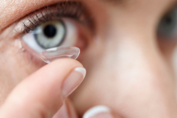 Nahaufnahme eines Auges einer Frau, die eine Kontaktlinse einsetzt mit ihrem Finger.