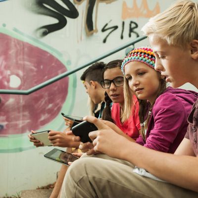 Eine Gruppe von Kindern sitzt vor einer Graffitiwand und schaut ins Handy.