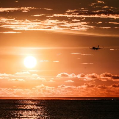 Sonnenuntergang über dem Meer, ein Flugzeug ist am Himmel sichtbar.