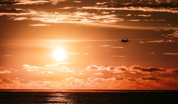 Sonnenuntergang über dem Meer, ein Flugzeug ist am Himmel sichtbar.